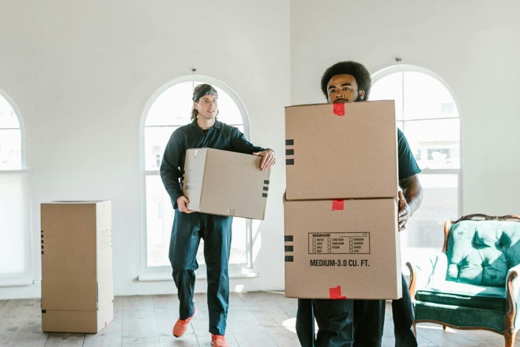 Two movers carrying boxes in a sunlit room, ready to assist with relocation.