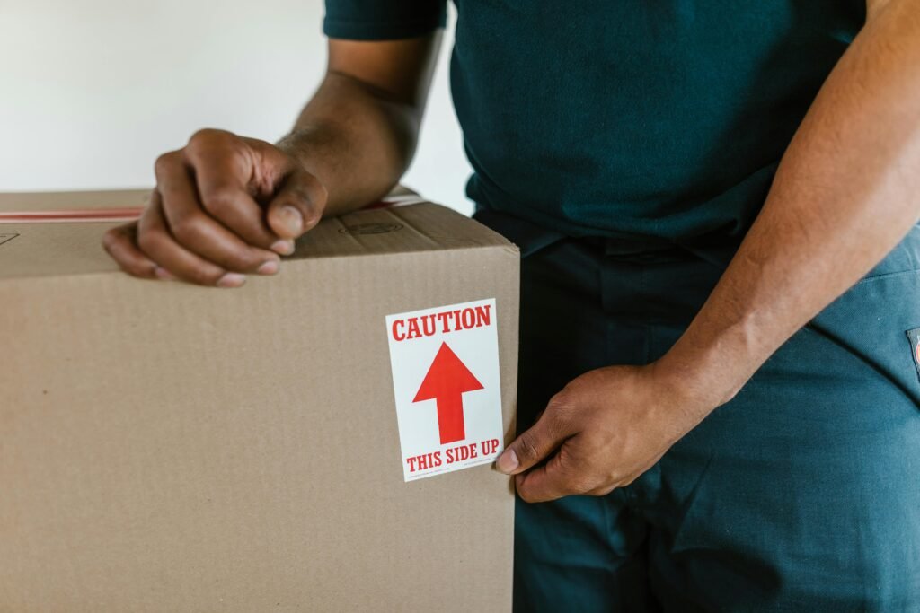 A person handling a moving box with a 'caution this side up' label indoors.